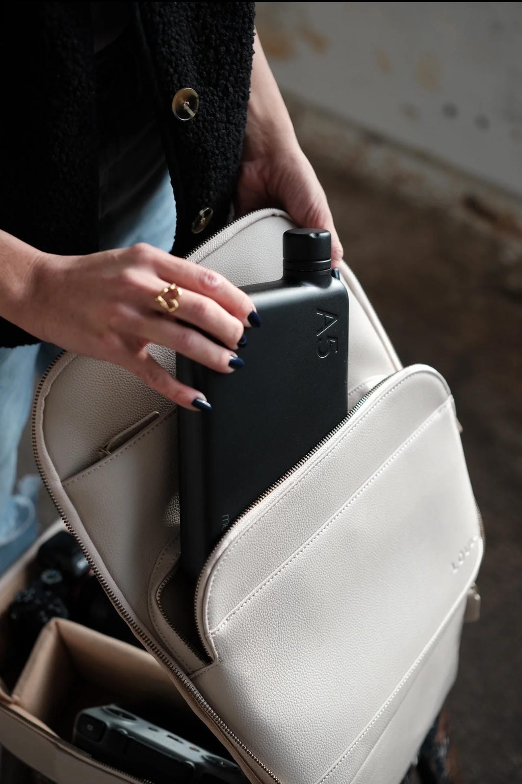 Person holding a black flask inside a beige leather bag.