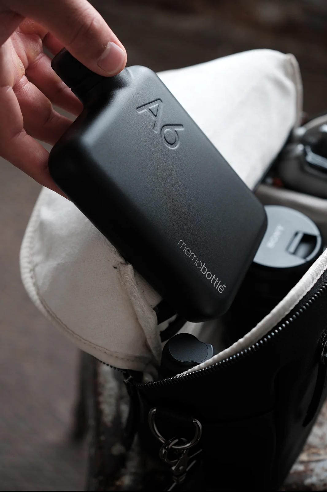 Person holding a black 'memoBottle' device in a bag