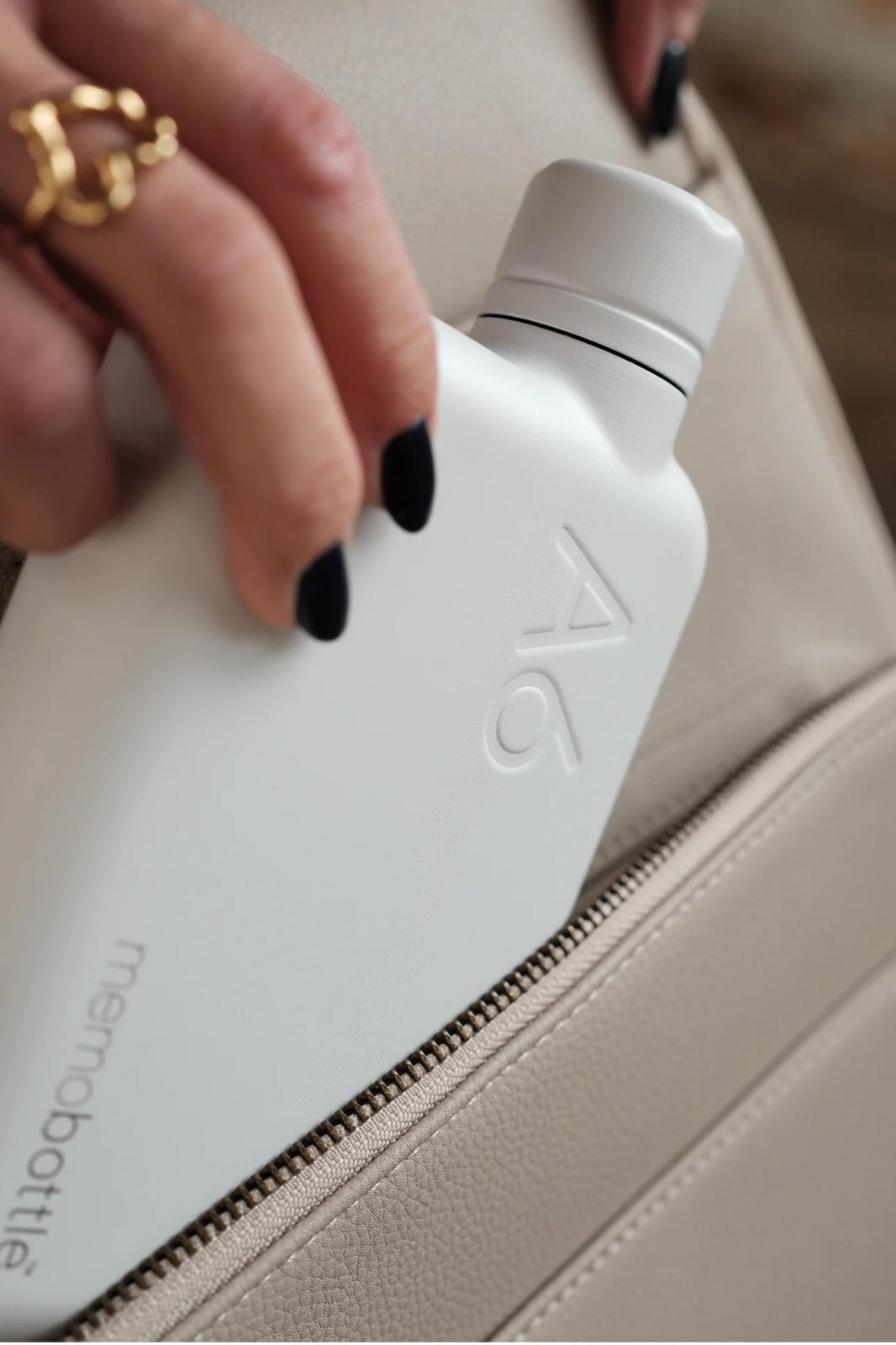 Person holding a white water bottle with 'memobottle' branding on a beige surface.