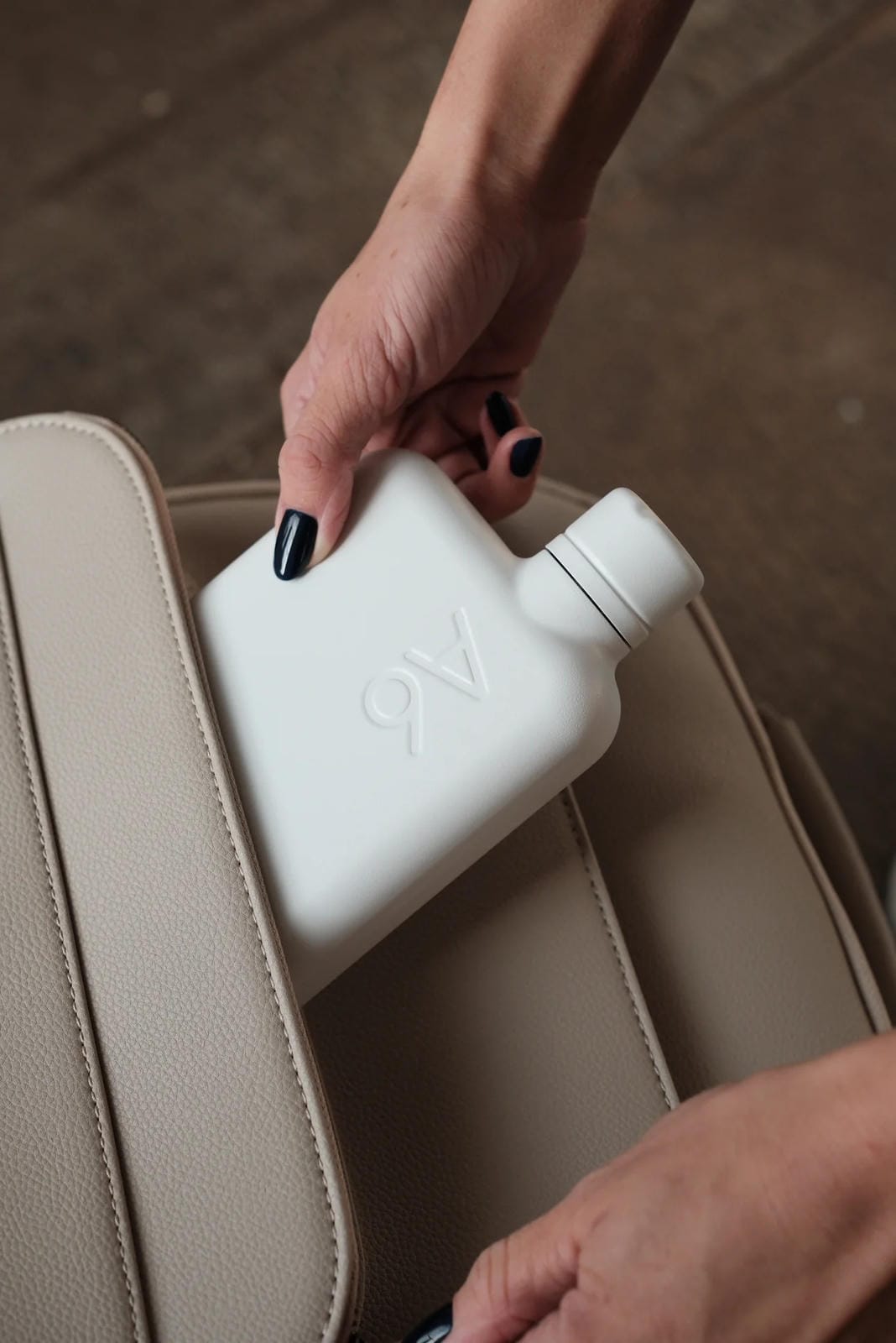Person holding a white bottle with '9V' branding on a beige car seat.