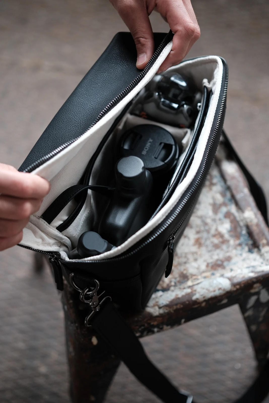 Black leather bag with a compartment containing a camera and lens on a textured surface.