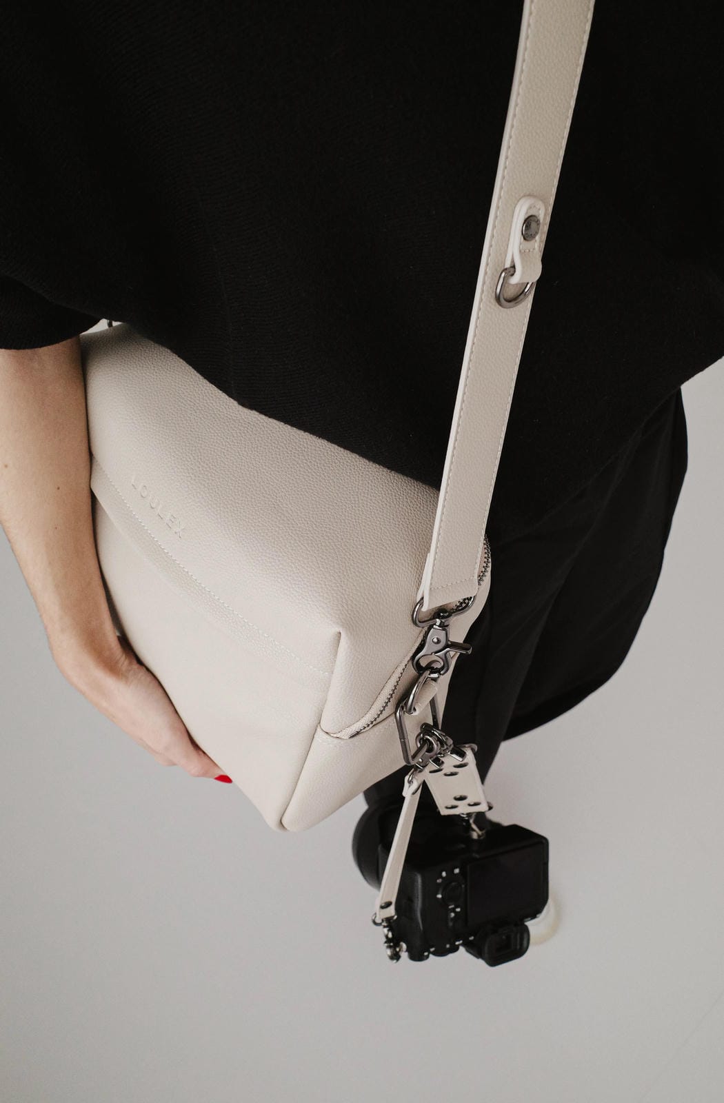 White handbag with a black strap held by a person on a gray background