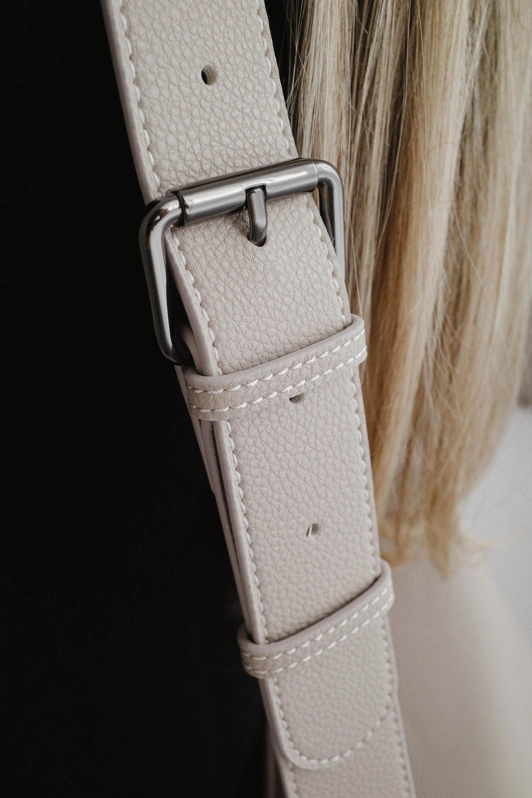 Close-up of a light gray leather strap with a silver buckle on a blurred background