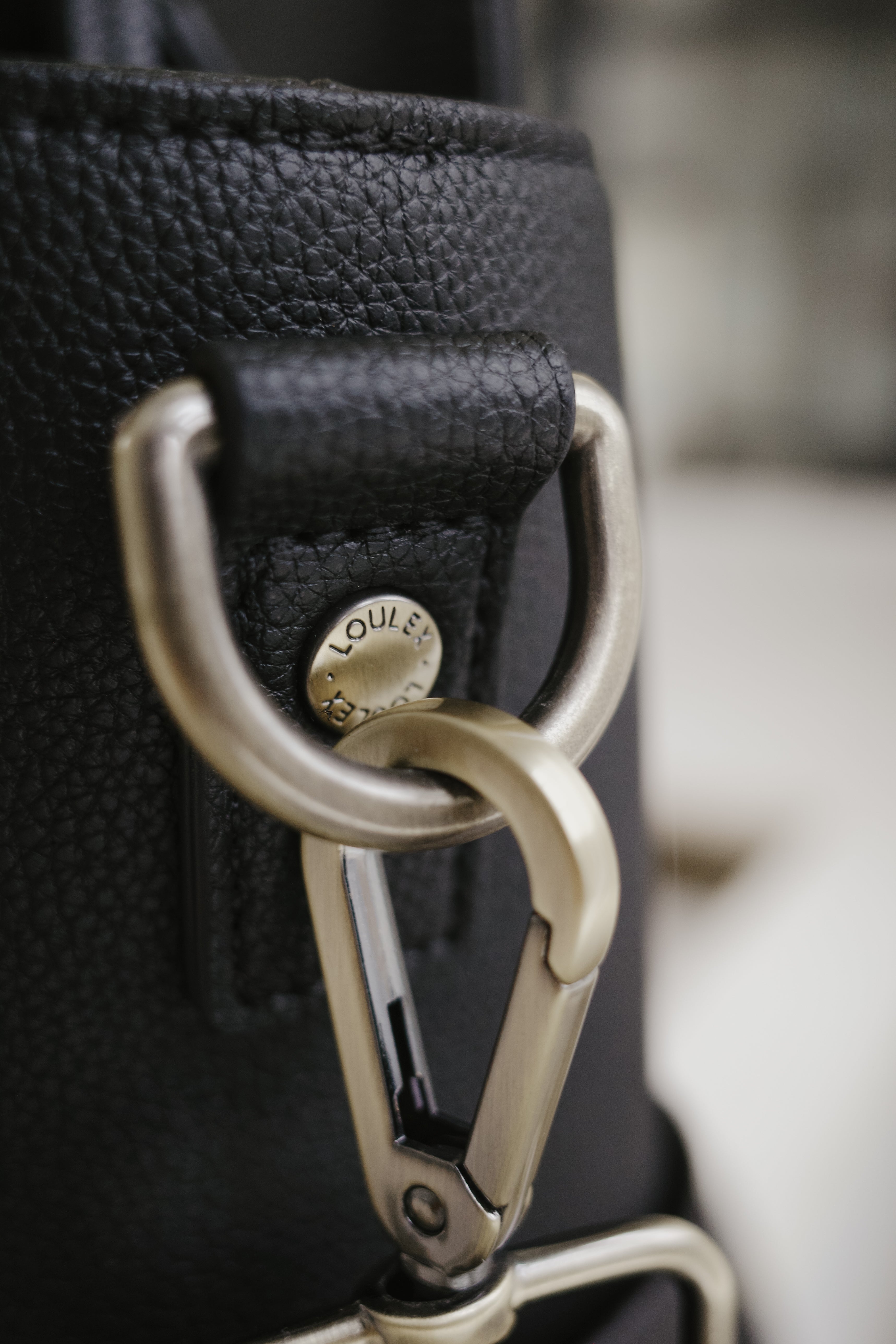 Gros plan sur un sac en cuir noir avec un mousqueton doré et le logo « Louis Vuitton ».