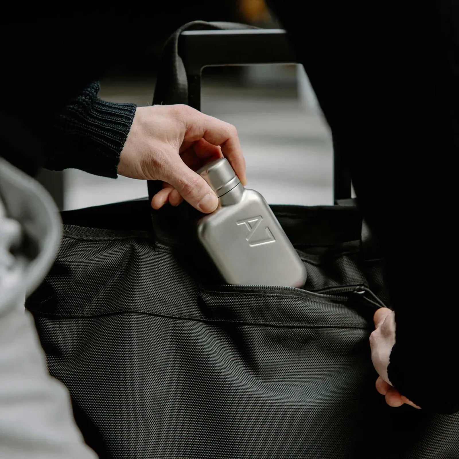 Person placing a metallic flask into a black bag